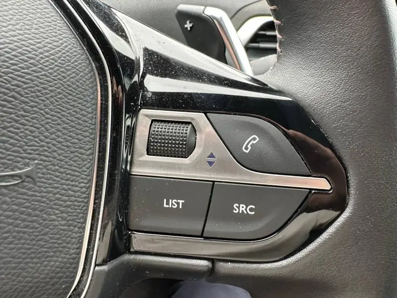 Gros plan sur les commandes gauche du volant cuir noir du Peugeot 3008 Hybride Rechargeable 2024, boutons LIST et SRC visibles.