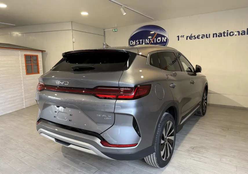 Vue 3/4 arrière droite du BYD SEAL U gris métallisé avec feux arrière LED et toit noir en intérieur showroom.