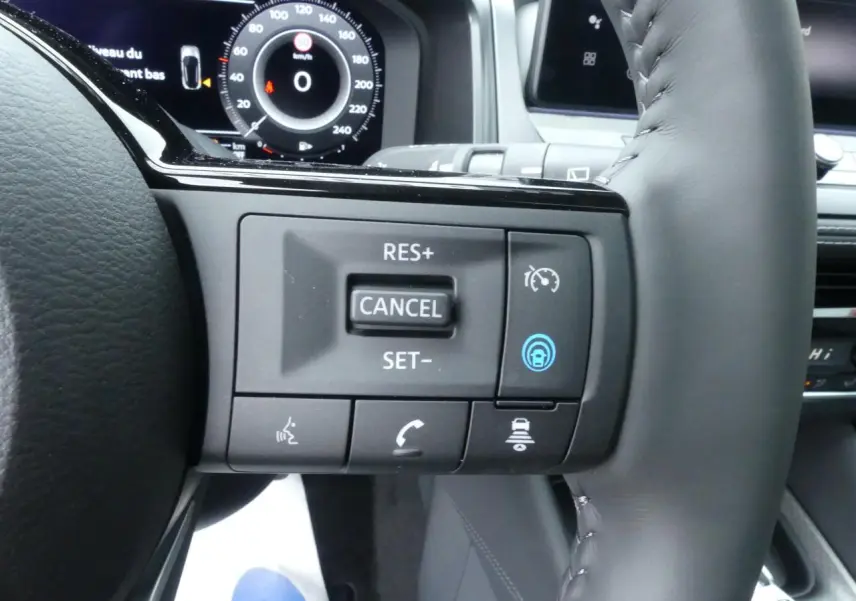 Gros plan sur les commandes au volant à droite du Nissan Qashqai 2025, avec affichage numérique du tableau de bord en arrière-plan.