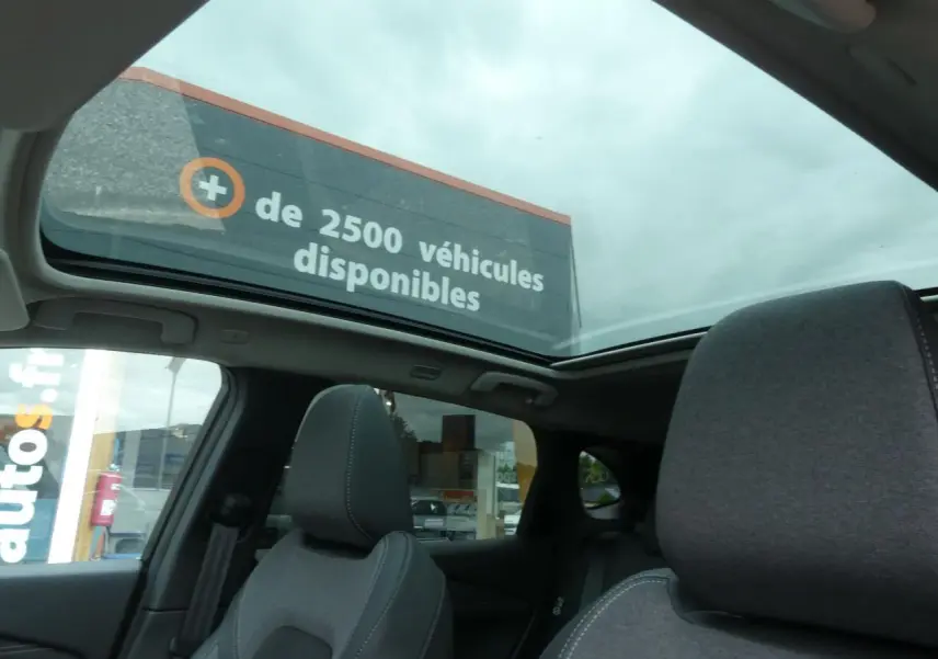 Toit panoramique ouvert montrant l'intérieur gris foncé du Nissan Qashqai 2025 côté arrière sous ciel nuageux.
