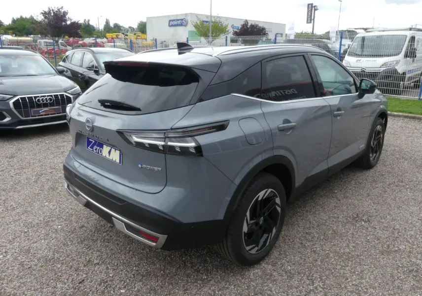 Vue 3/4 arrière droite du Nissan Qashqai gris métallisé avec toit noir et jantes alliage noires au stationnement.