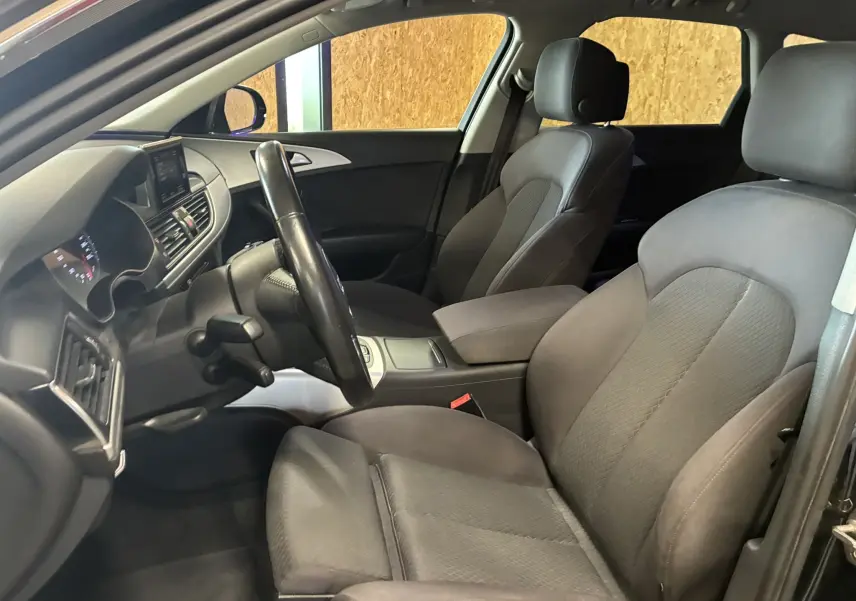 Vue intérieure côté conducteur de l'Audi A6 Avant noire 2017, sièges tissu noir et tableau de bord moderne.
