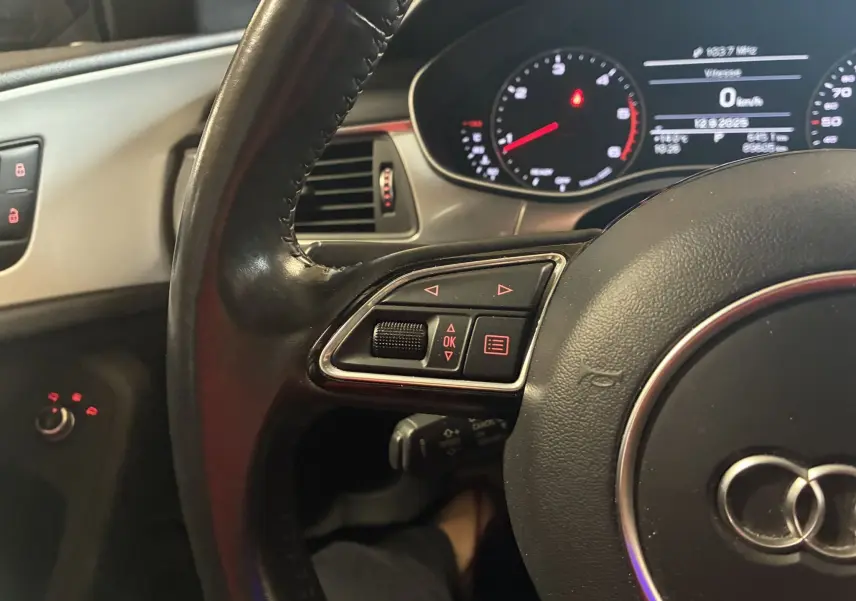 Gros plan sur le volant noir de l'Audi A6 Avant 2017 avec commandes intégrées et tableau de bord numérique allumé.