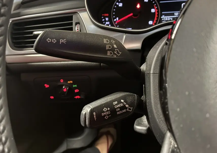 Gros plan intérieur sur les commandes au volant d'une Audi A6 Avant noire, mettant en valeur les leviers de clignotants et régulateur de vitesse.