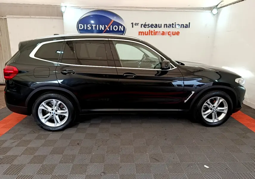 Profil côté droit d'un BMW X3 noir 2020, avec jantes alliage et vitres teintées, stationné en intérieur showroom.