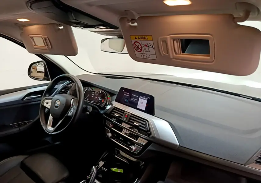 Vue intérieure côté conducteur du BMW X3 noir 2020, tableau de bord moderne avec écran tactile et volant multifonctions cuir.