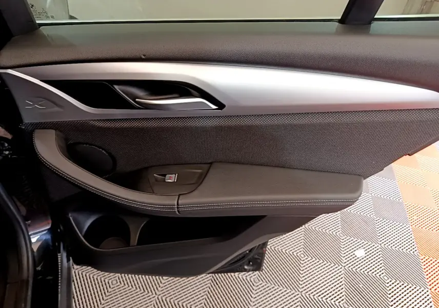 Vue intérieure côté gauche de la porte avant noire du BMW X3 xDrive20d 2020 avec insert argenté et bouton de vitre.