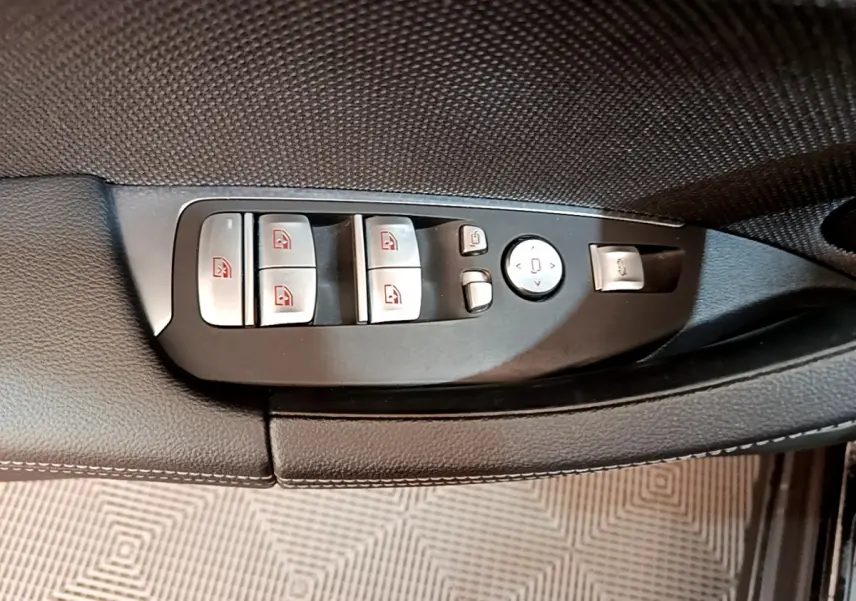 Gros plan sur les commandes de lève-vitres et rétroviseurs côté conducteur du BMW X3 noir 2020.