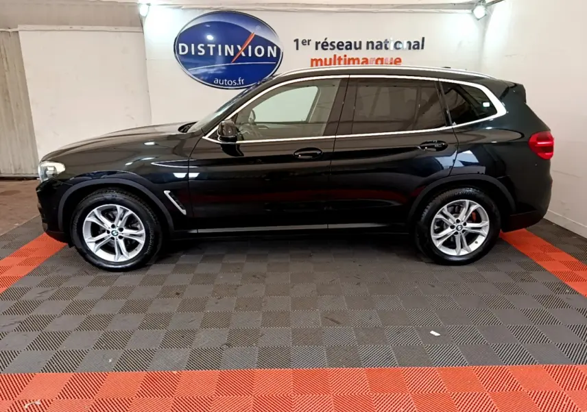 BMW X3 xDrive20d noir vue de profil côté gauche dans un showroom avec sol gris et bandes rouges.