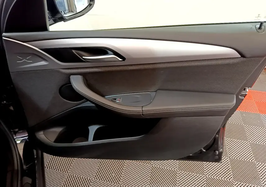 Porte intérieure côté gauche noire de BMW X3 xDrive20d 2020 avec insert argenté et logo X visible.
