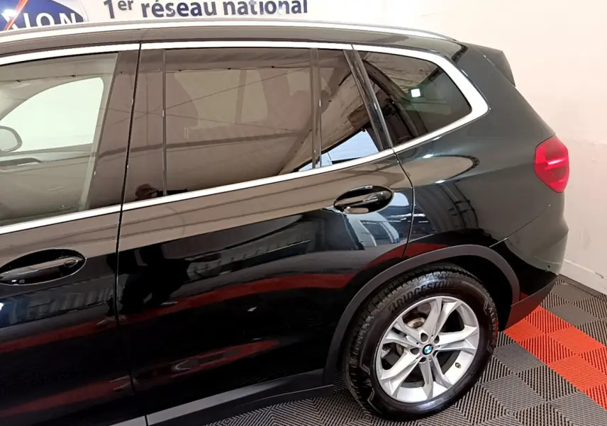 Vue latérale côté droit d'un BMW X3 noir avec jantes alliage et vitres teintées dans un showroom intérieur.