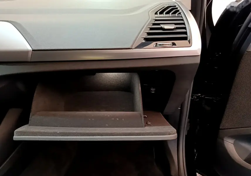 Gros plan sur la boîte à gants ouverte côté passager du BMW X3 xDrive20d noir, montrant le tableau de bord et la portière.