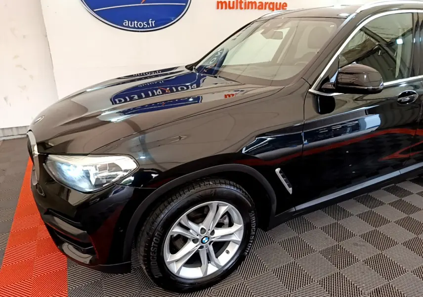 Vue 3/4 avant gauche d'un BMW X3 noir brillant avec jantes alliage et phares LED allumés.