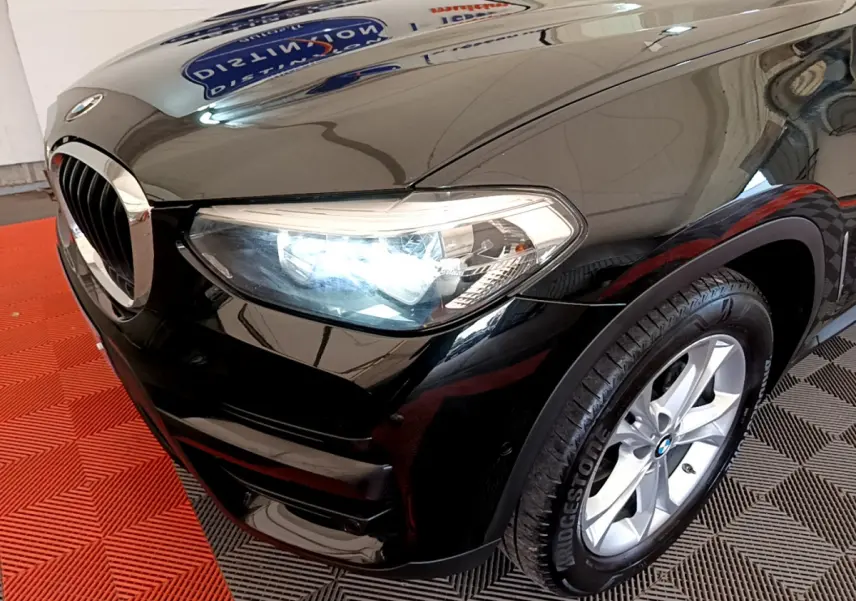 Gros plan sur l'avant droit noir d'un BMW X3 xDrive20d 2020 avec phare allumé et jante alu visible.