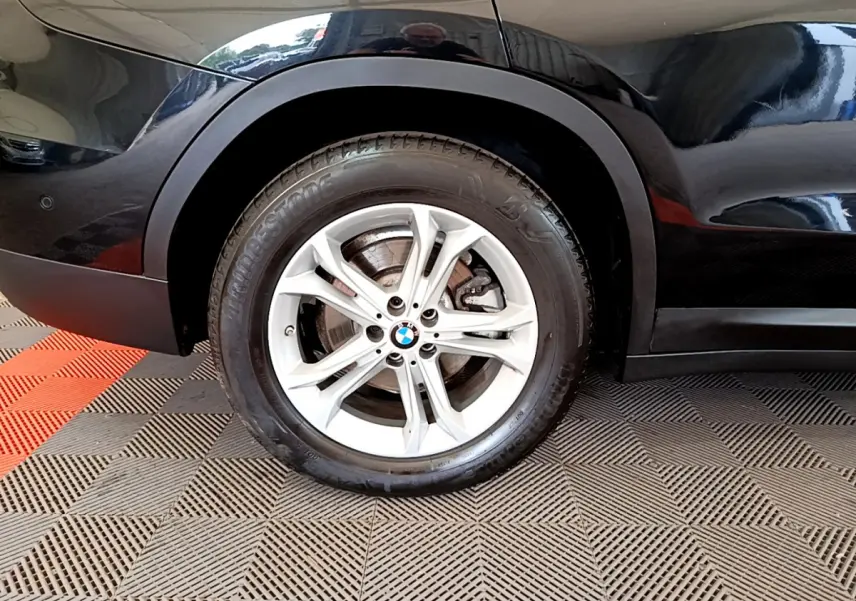 Gros plan sur la roue avant gauche d’un BMW X3 noir, avec jante alliage argent et logo BMW central.