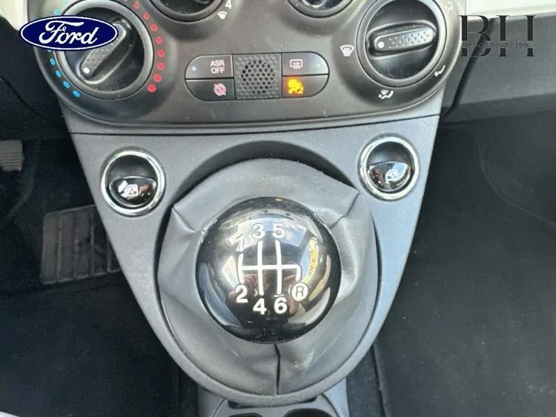 Le levier de vitesses manuel noir de la Fiat 500 blanche, vu en gros plan depuis l'intérieur avant.