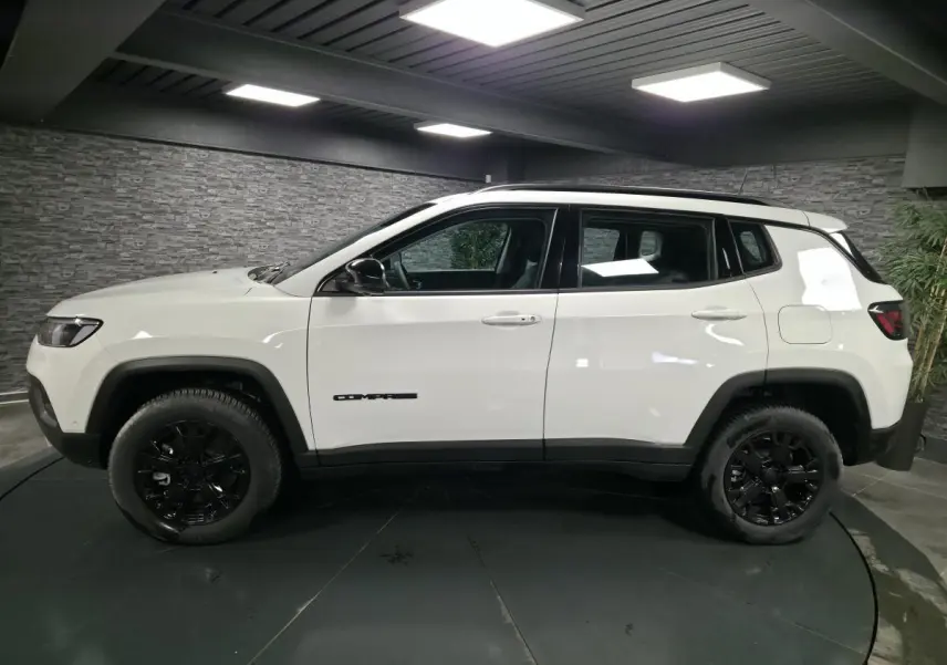Jeep Compass blanc vu de profil côté gauche, avec jantes noires et détails noirs contrastants.