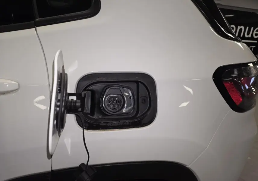 Prise de recharge ouverte côté gauche arrière d'un Jeep Compass blanc hybride rechargeable avec feu arrière visible.