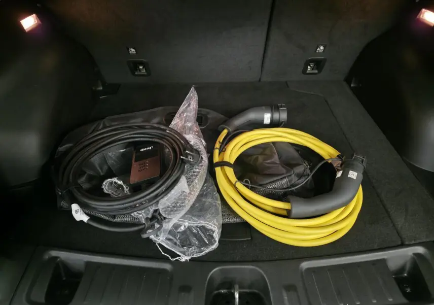 Coffre ouvert d'un Jeep Compass blanc 2024 montrant deux câbles de recharge, noir et jaune, sur tapis noir.