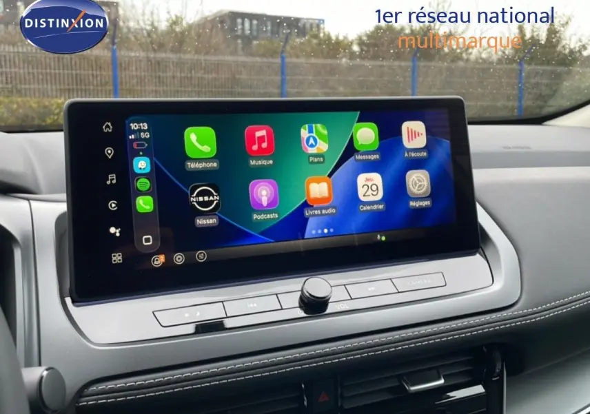 Écran tactile central du Nissan Qashqai 2025, affichant les applications Apple CarPlay, avec tableau de bord gris et coutures blanches.