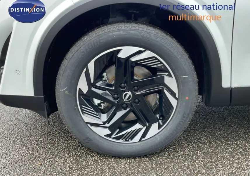 Gros plan sur la roue avant droite du Nissan Qashqai blanc nacré, mettant en valeur la jante noire et argentée au design moderne.