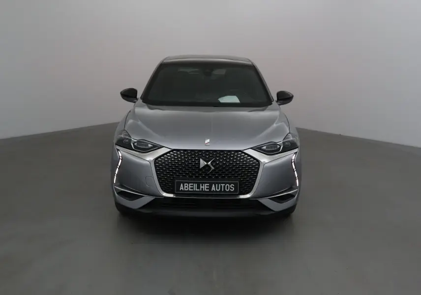 Vue frontale d'une DS3 Crossback E-TENSE gris Artense avec calandre distinctive et feux LED verticaux allumés.
