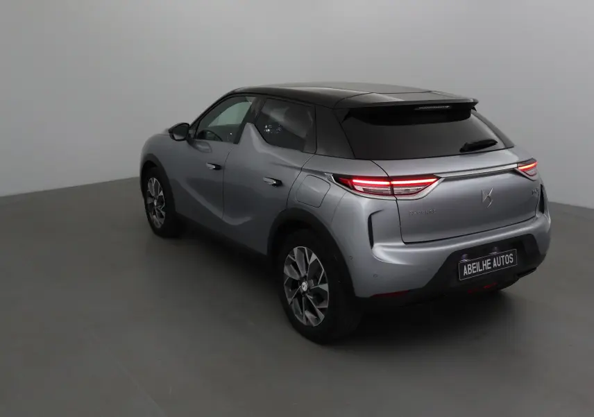 Vue 3/4 arrière droite d'un DS3 Crossback E-TENSE gris Artense avec feux arrière allumés dans un studio.