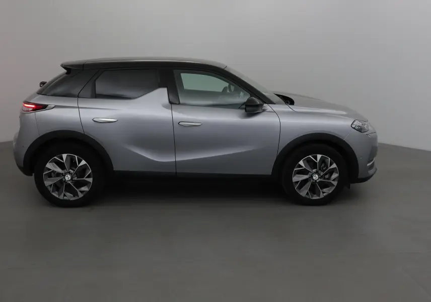 Vue de profil côté gauche du DS3 Crossback E-TENSE gris Artense avec toit noir et jantes stylisées.