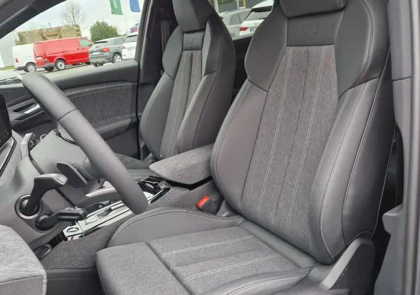 Vue intérieure côté conducteur de l'Audi Q6 e-tron Performance S-Line 2025 avec sièges sport gris Manhattan et surpiqûres contrastées.