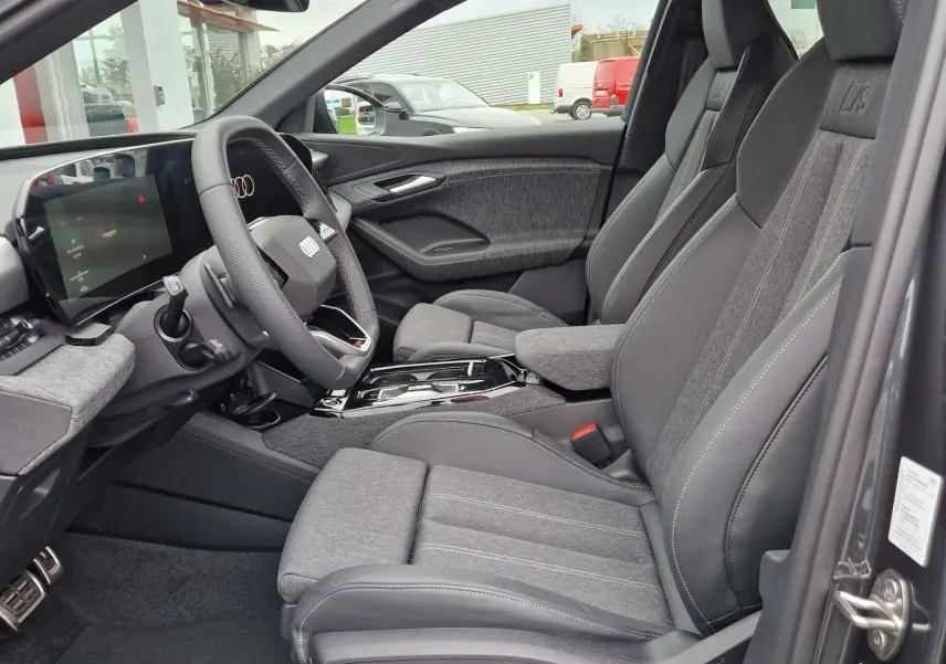 Intérieur côté conducteur de l'Audi Q6 e-tron Performance S-Line gris Manhattan, sièges sport avec logo S et tableau de bord numérique.