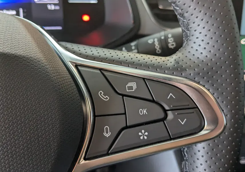 Gros plan sur les commandes du volant en cuir perforé du Renault Captur gris Cassiopée 2025, version hybride.