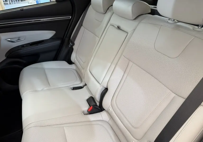 Vue latérale des sièges arrière en cuir beige clair du Hyundai Tucson 2022, avec ceinture de sécurité et porte noir.