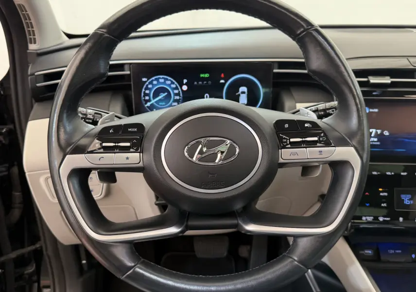 Vue rapprochée du volant cuir noir du Hyundai Tucson 2022 avec commandes multifonctions et tableau de bord digital.