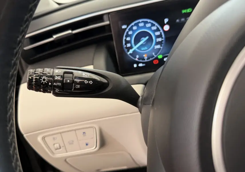 Gros plan sur la manette de feux et clignotants à gauche du volant d'un Hyundai Tucson noir, avec tableau de bord numérique visible.