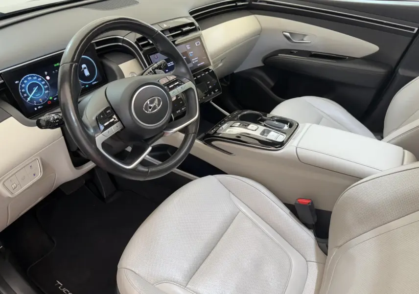 Intérieur clair du Hyundai Tucson 2022 vu côté conducteur, avec volant cuir et tableau de bord digital.