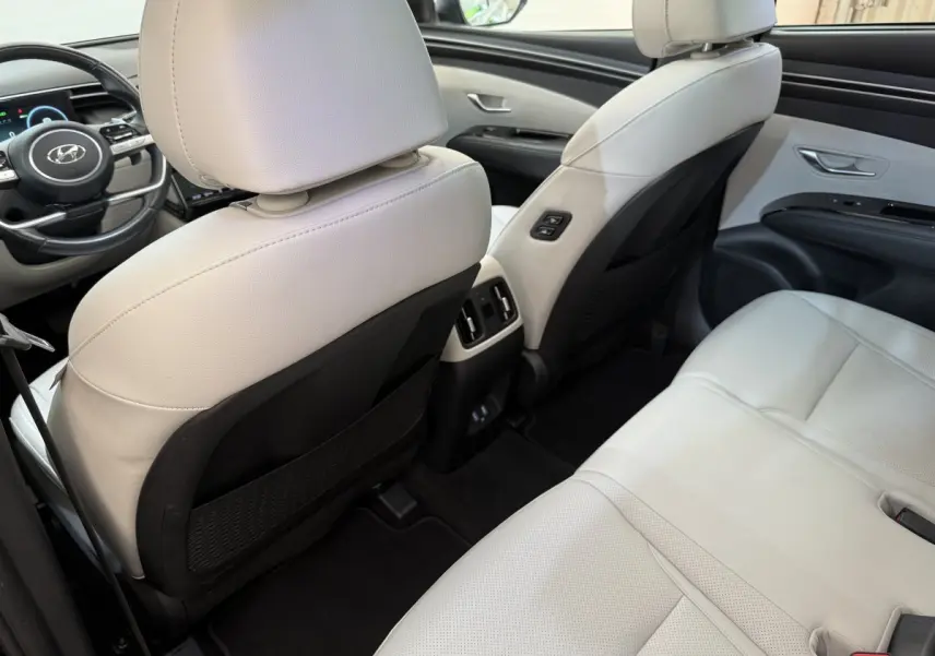 Vue arrière intérieure du Hyundai Tucson 2022 hybride rechargeable, sièges cuir blanc et console centrale avec aérateurs.
