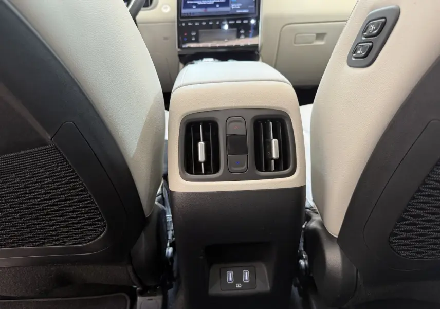 Vue rapprochée de la console centrale arrière beige et noire du Hyundai Tucson 1.6 PHEV avec commandes de climatisation et ports USB.