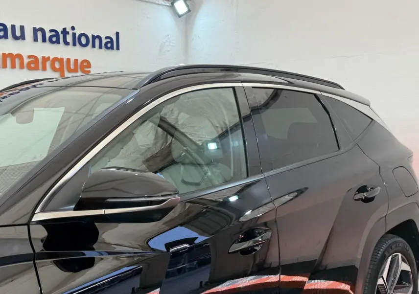 Profil côté gauche du Hyundai Tucson noir 2022 avec rétroviseur et poignées de porte visibles en intérieur showroom.