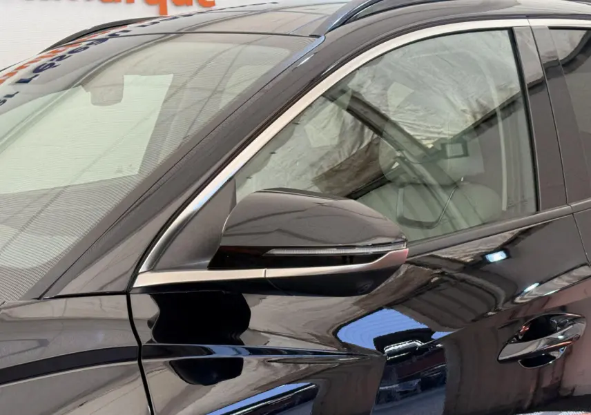 Gros plan sur le rétroviseur côté gauche d’un Hyundai Tucson noir brillant avec détails chromés et vitre avant visible.