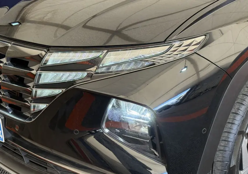 Gros plan sur l'avant droit noir brillant du Hyundai Tucson 2022, mettant en valeur ses phares LED et la calandre distinctive.