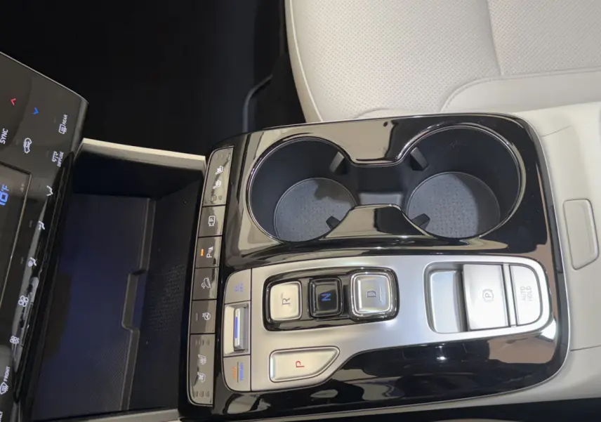 Gros plan sur la console centrale noire brillante du Hyundai Tucson 2022 avec commandes de boîte auto et porte-gobelets.
