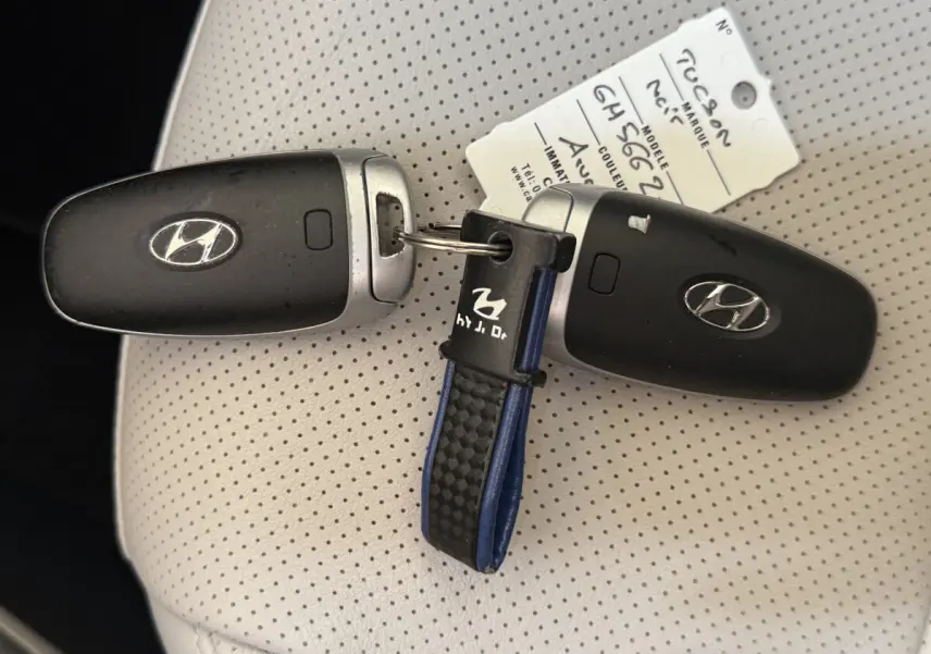 Gros plan sur deux clés noires Hyundai Tucson posées sur un siège en cuir perforé beige avec étiquette d'identification.