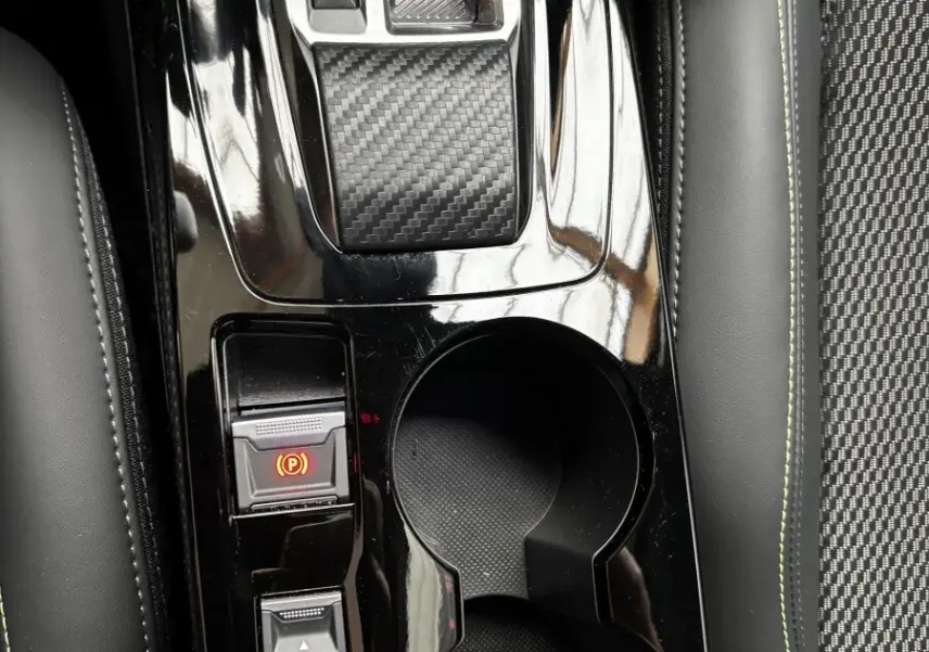 Vue rapprochée de la console centrale noire brillante de la Peugeot 208 Hybrid 110 e-DCS6 GT avec levier de vitesses et porte-gobelets.