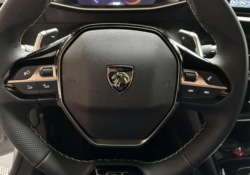 Gros plan sur le volant cuir et alu de la Peugeot 208 Hybrid 110 e-DCS6 GT avec logo lion et commandes intégrées.