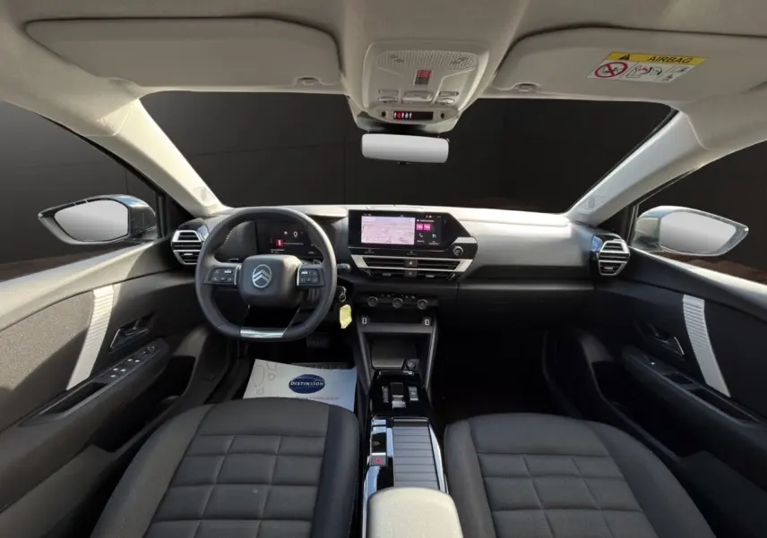 Intérieur de la Citroën C4 Hybride 2025 vu de face, tableau de bord moderne avec écran tactile et sièges gris foncé.