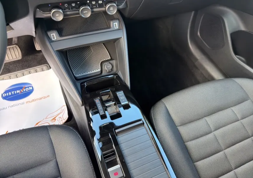Vue intérieure centrée sur la console centrale noire brillante et les sièges tissu gris foncé d'une Citroën C4 hybride 2025.