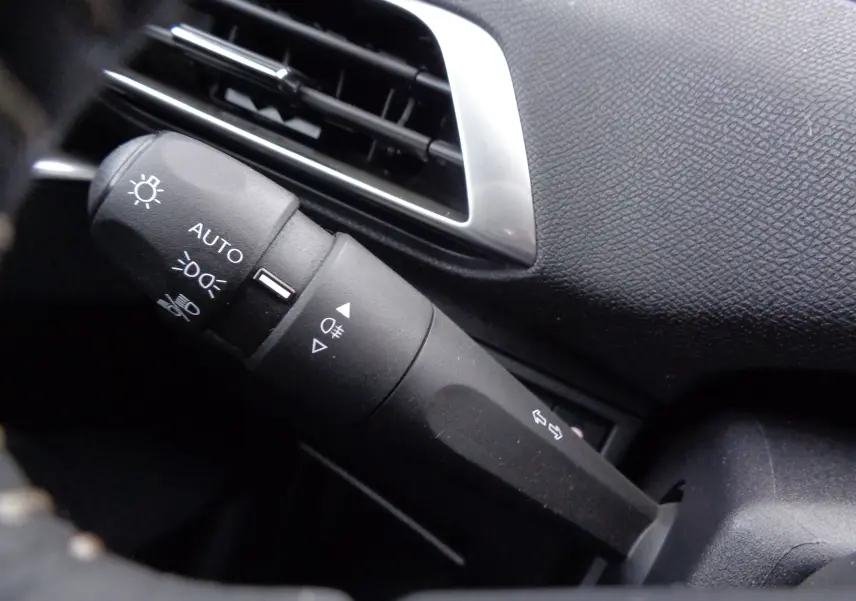 Gros plan sur la commande des feux automatiques et antibrouillard dans l'habitacle noir du Peugeot 5008 2023.