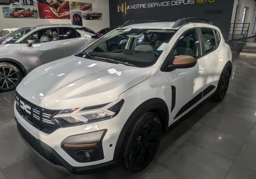 Vue 3/4 avant droit d'une Dacia Sandero Stepway TCe 110 blanc glacier avec rétroviseurs bronze et jantes noires en showroom.