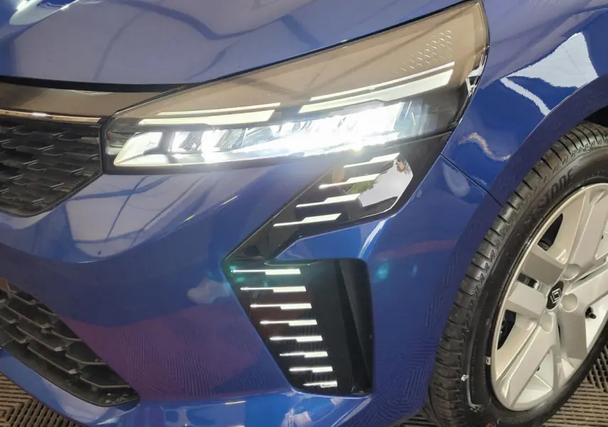 Gros plan sur l'avant droit d'une Renault Clio bleu 2025, mettant en valeur les phares LED et la jante alu.