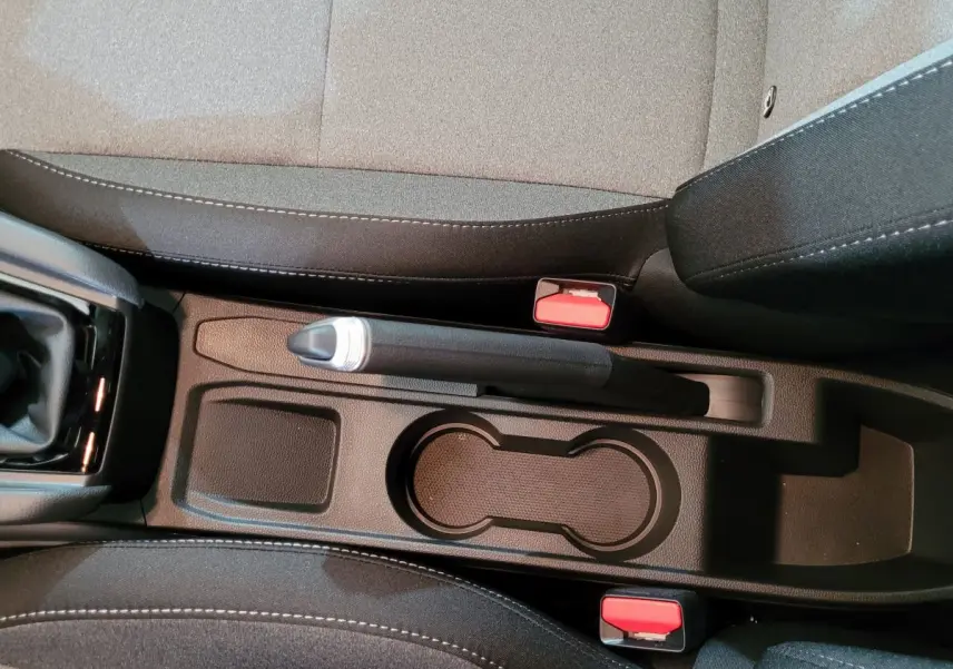 Vue plongeante sur la console centrale noire de la Renault Clio bleu, avec frein à main manuel et porte-gobelets.